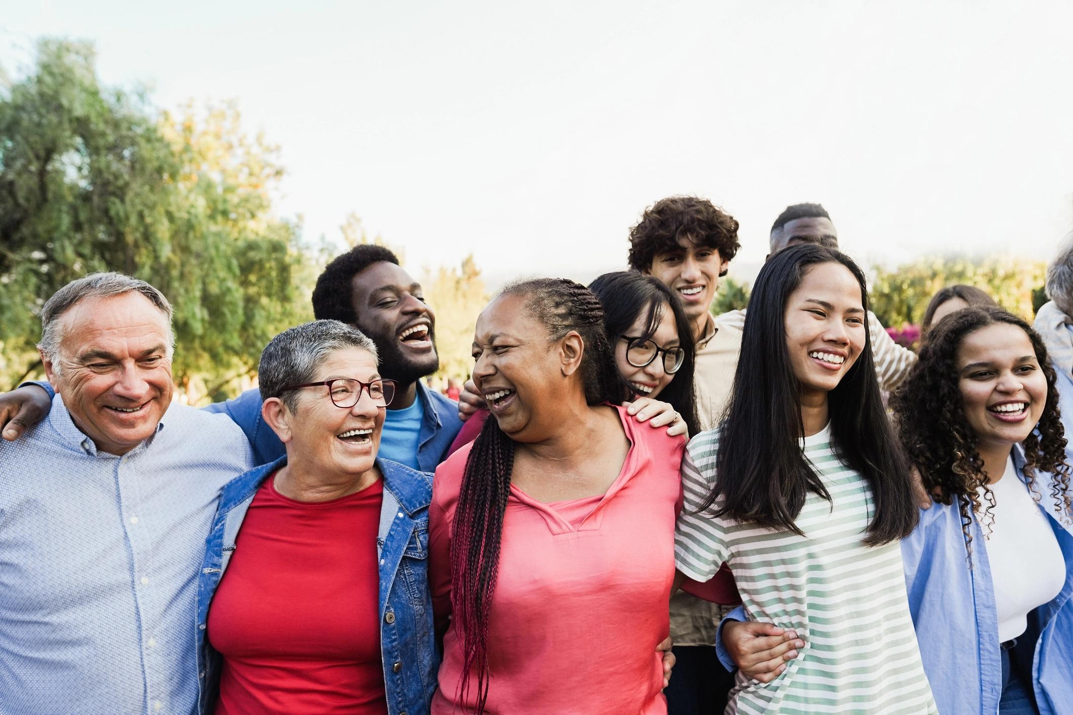 A diverse group of smiling people standing closely together outdoors.