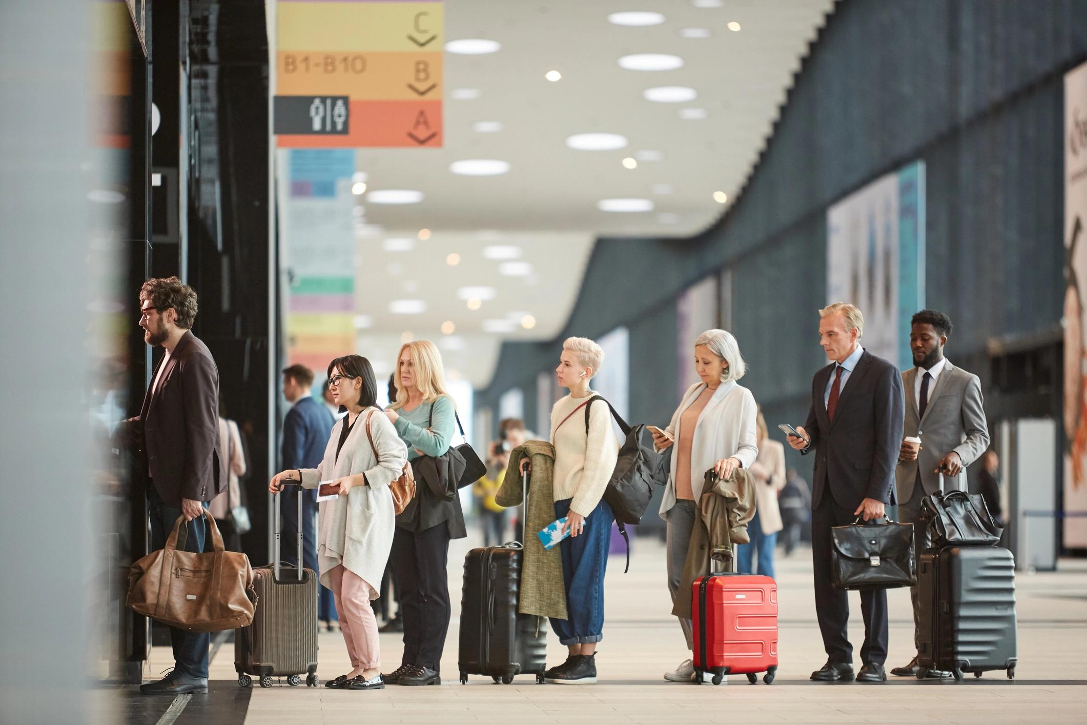 People of various ethnicities standing in line with luggage at an airport.