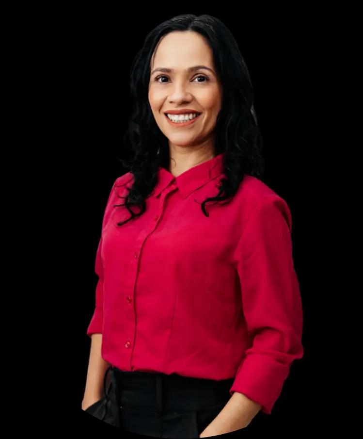 A woman with medium skin tone and long dark curly hair, wearing a pink blouse. She is smiling warmly.