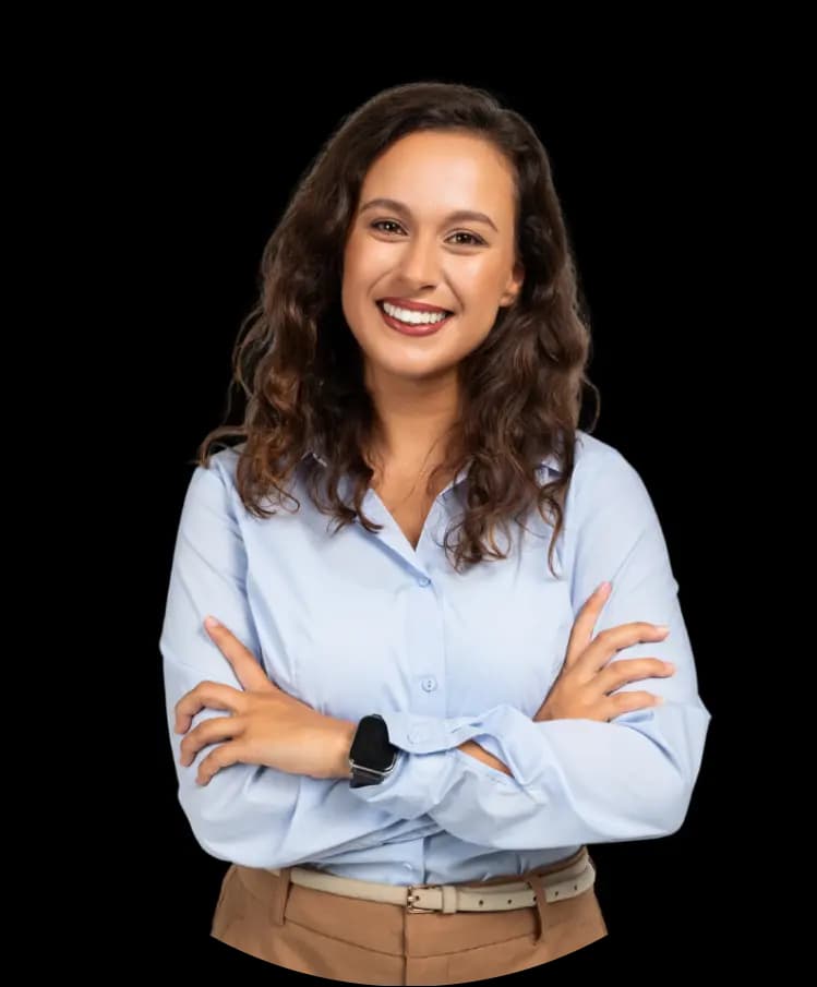 A young woman with medium skin tone and long curly hair, wearing a light blue blouse. She is smiling brightly with her arms crossed.