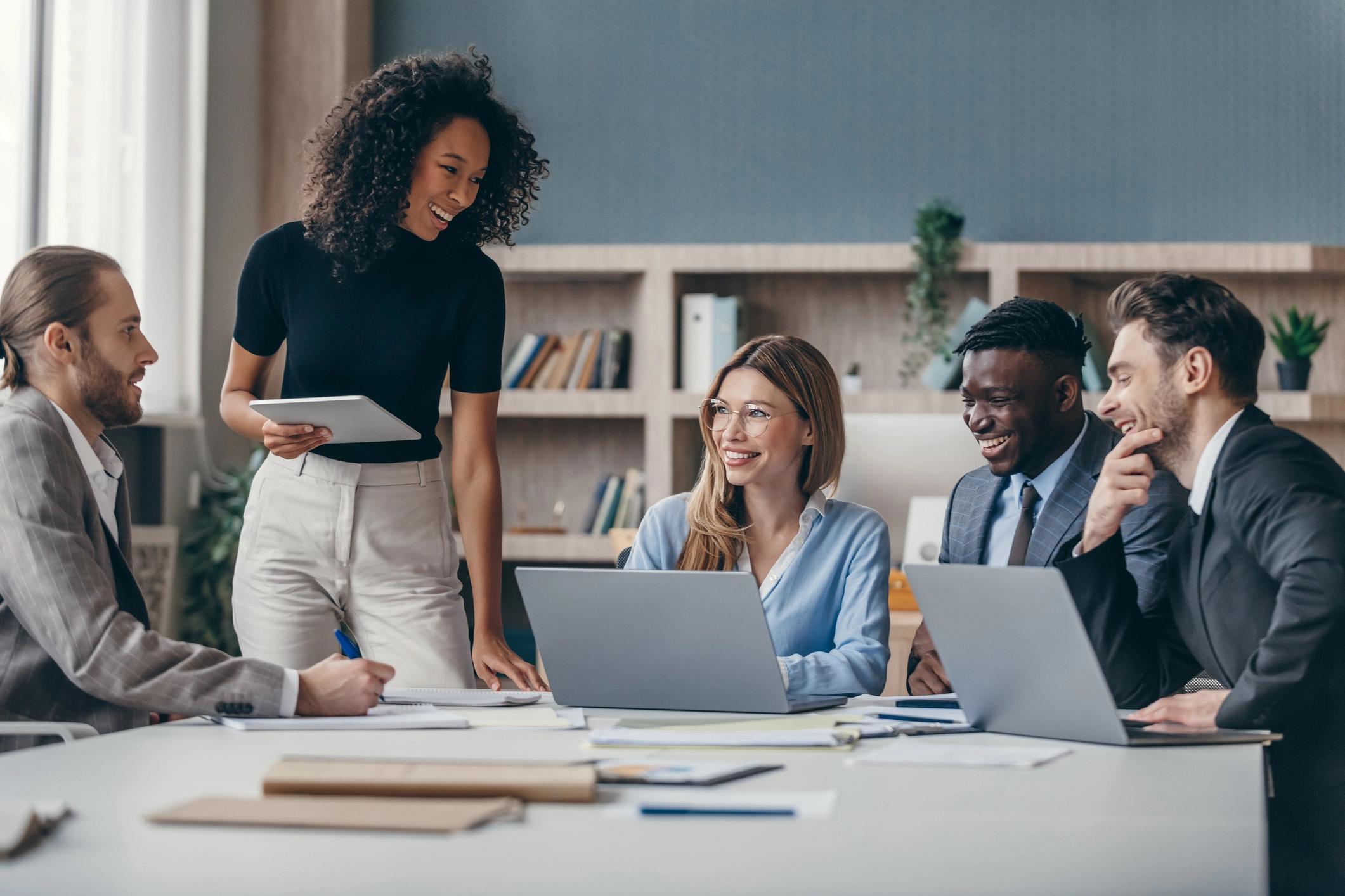 A diverse group of five professionals engaging in a lively discussion around a conference table in a modern office setting